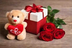 Peluche con corazón, caja de regalo roja y rosas sobre una mesa, imagen representativa del 14 de febrero
