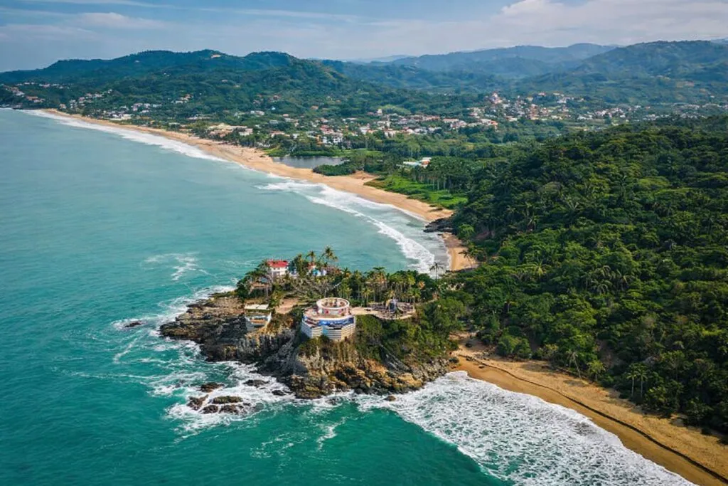 Vista aérea fotorealista de la costa de Riviera Nayarit con playas del Pacífico, acantilados y vegetación abundante en un paisaje turístico moderno.