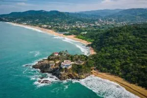 Vista aérea fotorealista de la costa de Riviera Nayarit con playas del Pacífico, acantilados y vegetación abundante en un paisaje turístico moderno.