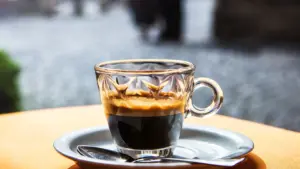 Taza de café recién preparado junto a granos tostados en una cafetería.