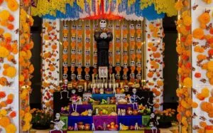 Puesto de mercado mexicano con flores de cempasúchil, frutas, veladoras y artículos tradicionales para las ofrendas de Día de Muertos.