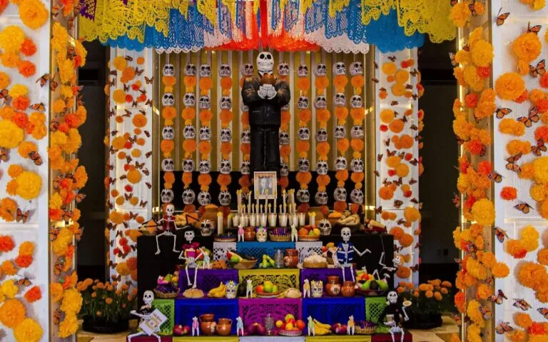 Puesto de mercado mexicano con flores de cempasúchil, frutas, veladoras y artículos tradicionales para las ofrendas de Día de Muertos.